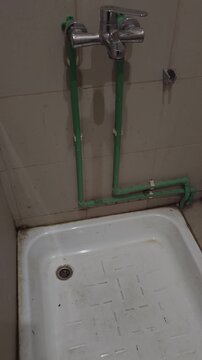 Old bathroom with exposed water pipes, worn shower tray and outdated plumbing fixtures showing aging residential interior and utility systems