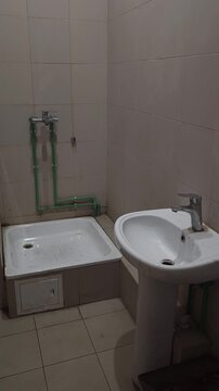 Old bathroom interior with exposed plumbing, worn shower tray and ceramic sink showing aging residential utilities and outdated sanitary fixtures