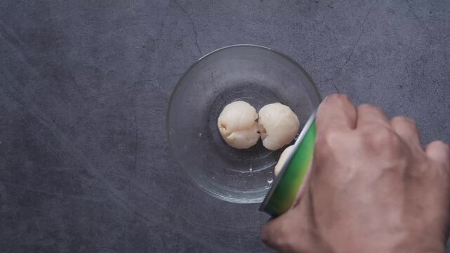 Pouring fresh lychees from can into bowl for sweet dessert preparation