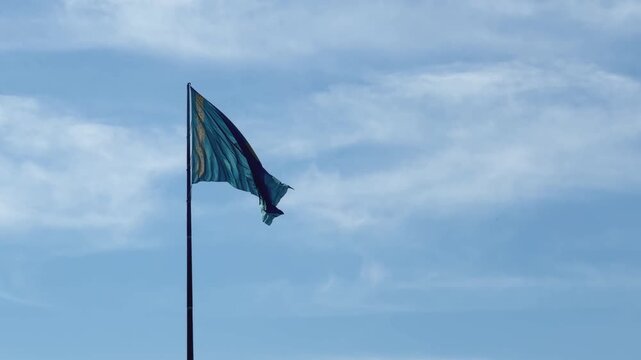 Kazakhstan national flag at State Symbols Square, with large blue fabric, golden emblem and summer foliage beneath open sky, shot handheld. High quality 4k footage