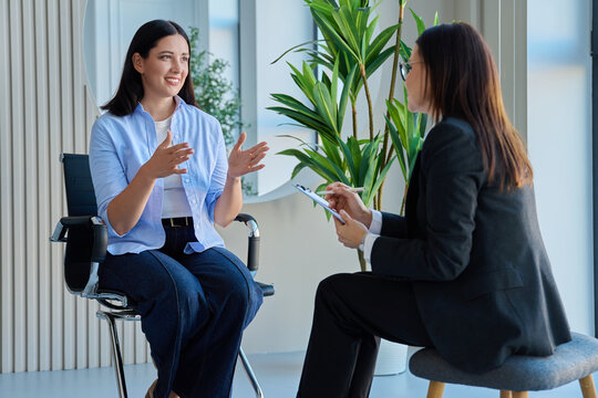 Female candidate talking to HR manager with clipboard during job interview in office