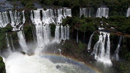 Aerial view of roaring multi-tiered waterfall wall with a rainbow in the mist at Iguazu © Travelwavi