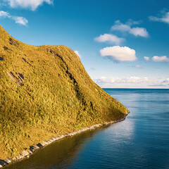 High angle vertical view of sunny mountain coast extending into blue ocean under bright sky with clouds in scandinavia with copy space © Quality by Simon