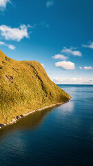 High angle vertical view of sunny mountain coast extending into blue ocean under bright sky with clouds in scandinavia with copy space © Quality by Simon