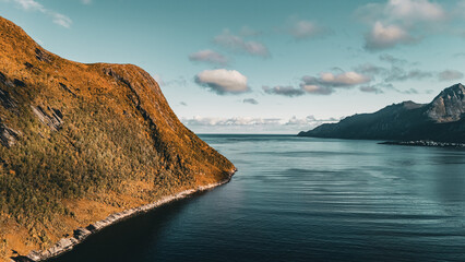Panoramic aerial drone view of autumn mountain coastline and fjord opening to the ocean under cloudy sky in Senja Norway with copy space © Quality by Simon