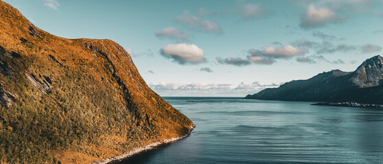 Panoramic aerial drone view of autumn mountain coastline and fjord opening to the ocean under cloudy sky in Senja Norway with copy space © Quality by Simon