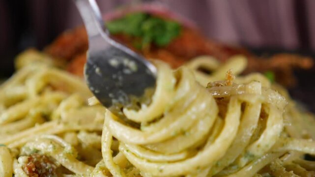 Close up cinematic shot of fresh pasta with green pesto sauce being lifted from a plate by a fork, capturing the creamy texture and vibrant color of the dish