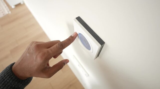 Person adjusting smart home digital thermostat on white wall for temperature control