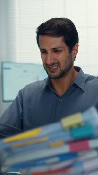 Vertical Screen : Stressed young Latin businessman having heart attack with severe chest pain at office desk. Cardiac arrest emergency, overworked burnout, medical stroke, health insurance crisis.