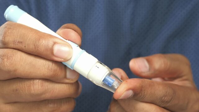Person using glucose lancet pen to prick finger for blood sugar testing at home