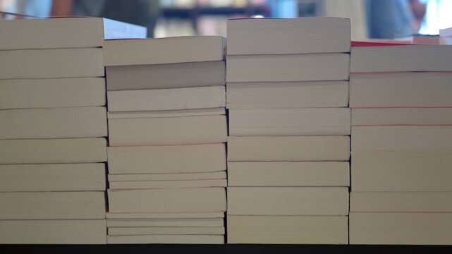 Close up of book stacks on shelf in bookstore with blurred background people walking by