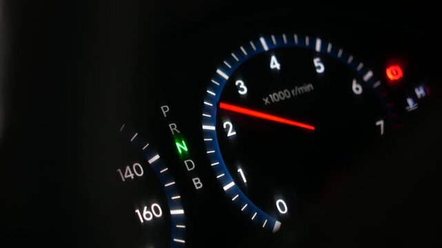 Close up shot of modern car dashboard with illuminated speedometer and tachometer gauges as engine starts and rpms rise