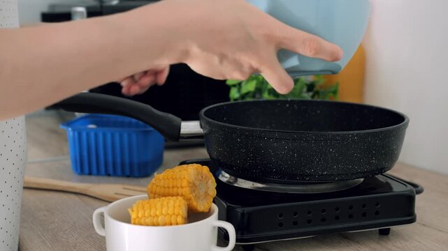 Person prepares dinner meal while pouring chopped vegetables into frying pan, coping with kitchen burnout. Cook empties blue container with ingredients over hot stove during daily routine.