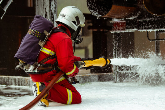 Firefighter spraying chemical foam hose to extinguish industrial plant fire