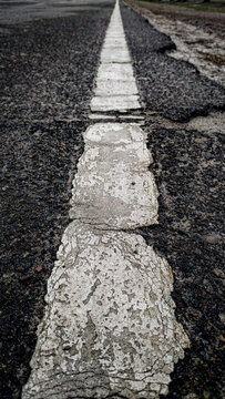 Close up of cracked white road marking line on old asphalt surface