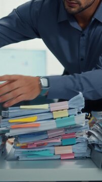 Vertical Screen : Overworked young Latin businessman read document in large stack of paperwork files at office desk. Tax audit deadline, accounting stress, corporate burnout, bookkeeping, bureaucracy.