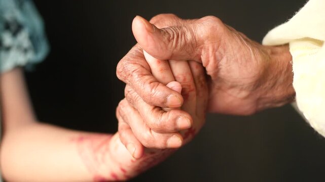 Close up of an elderly woman holding hands with child representing intergenerational connection and care