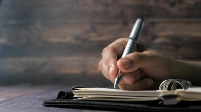 Person's hand holding pen writing on notebook close up motion footage