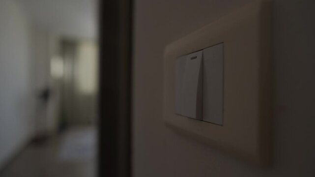 Reducing power consumption at home, close up of wall switch as man switches off unnecessary lights to avoid wasting electricity, blurred figure in background