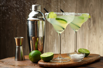 Obraz premium Delicious margarita cocktail in glasses, fresh fruits, salt, shaker and jigger on wooden table