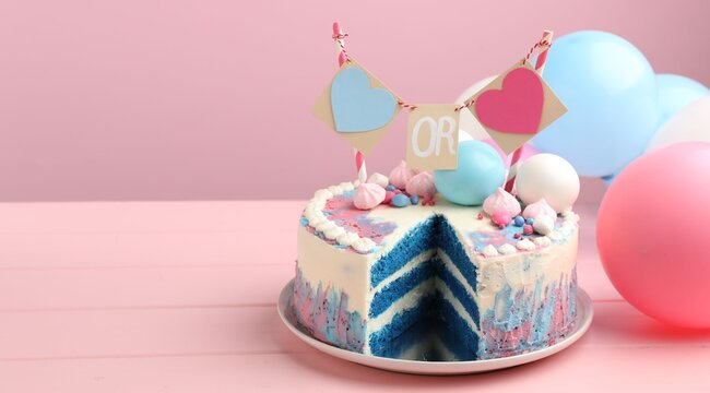 Decorated gender reveal cake with blue layers and balloons on pink wooden table. Space for text
