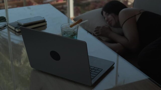 Laptop in focus with tired female freelancer sleeping in the background at a cafe, showing digital wellbeing, screen time, work fatigue and need for rest