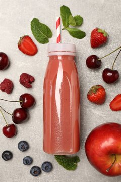 Delicious smoothie in bottle and fresh ingredients on light grey textured background, flat lay