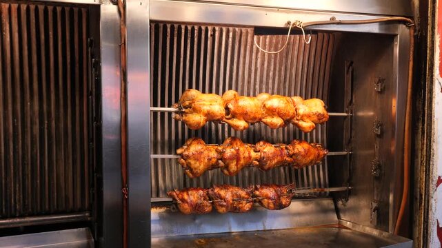Rotisserie chickens roasting on industrial spits in commercial kitchen oven with glowing flames