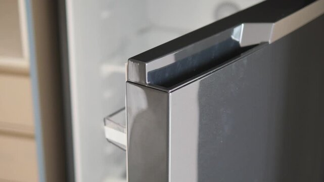 Close-up slow motion of open refrigerator door with chrome handle and interior light