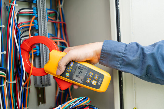 Cabinet inspection at a substation shows an engineer measuring current with a clamp meter on wiring inside a control cabinet.