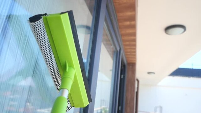 Cleaning glass window with squeegee and scrubber tool on sunny day