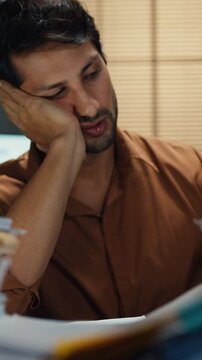 Overworked young Latin businessman waking from sleep nap to rush paperwork at desk in dark night office. Working late deadline burnout, heavy workload stress, and exhausted corporate problem concept.