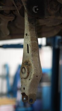 A rusty car rear lower control arm hanging from subframe.