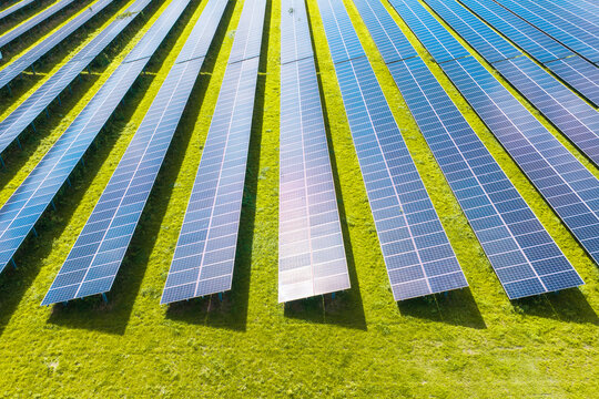 Solar panels installed in a large green field generating clean energy. Aerial view. Autonomous solar power station in a rural landscape.