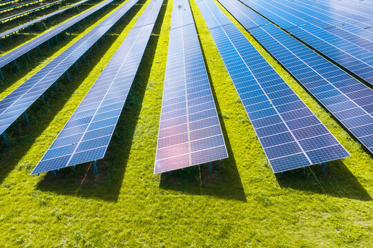Solar panels installed in a large green field generating clean energy. Aerial view. Autonomous solar power station in a rural landscape.