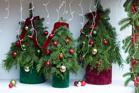 Festive Christmas tree arrangement with lush evergreen branches, red and gold ornaments, velvet ribbons and glowing fairy lights creating an elegant holiday celebration atmosphere indoors