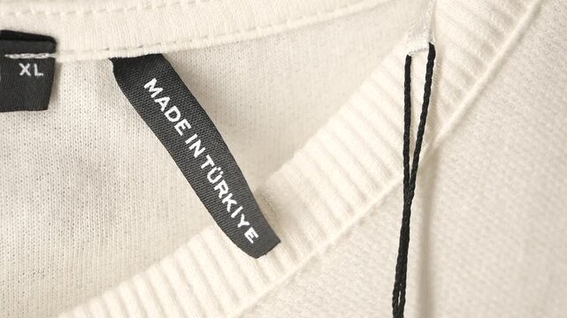 Close-up shot of a white sweater with a black label, made in T&uuml;rkiye, displaying the size as XL and regular fit