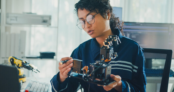 Young African American female robotics engineer discussing mechanical part on video call in laboratory. Remote work, virtual training, online meeting, future technology, technical support concept.