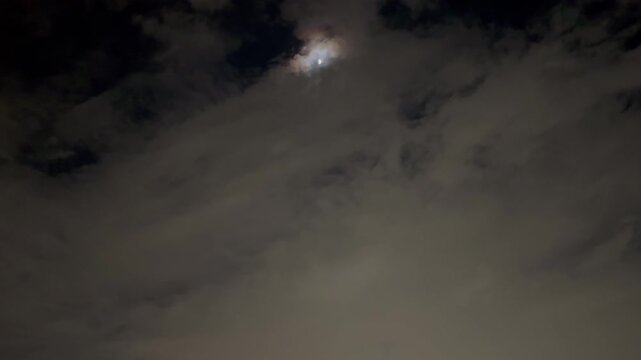 Static shot of the moon hidden behind distant clouds in a spooky Halloween night sky.