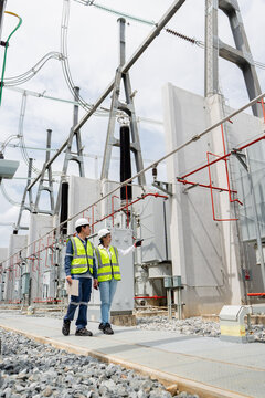 Transformer inspection at a substation shows two technicians standing beside a power transformer bay with red fire piping.