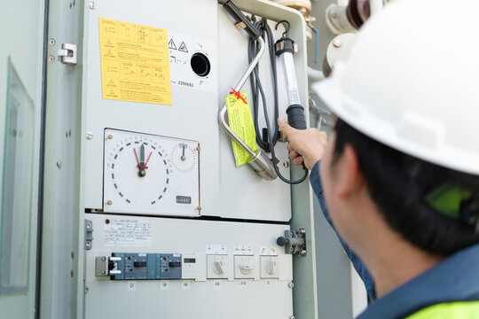 Performing a substation inspection of the control cabinet, a technician wearing a hard hat carefully checks an internal gauge.