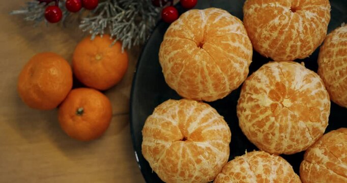 Mandarin fruit portions gather on dark plate near unpeeled citrus during festive dining setting, illustrating citrus allergy risk alongside winter evergreen branches and bright berries.