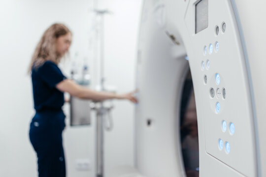 Close view of CT scanner control panel with female healthcare worker blurred in background, concept of diagnostic imaging, radiology and medical technology.