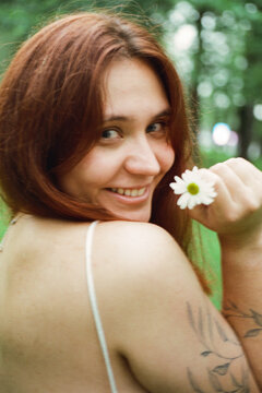 A woman glances back with a daisy in a summer park