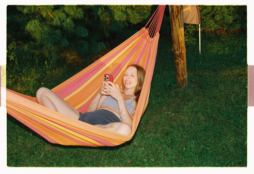 A woman scrolls her phone and laughs in the backyard