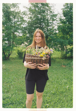 A woman holds a wicker basket of wildflowers in a garden