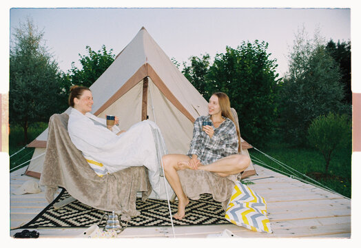 Friends laughing over hot drinks at a summer glamping site