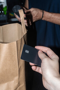 Hand Holding a Card Near a Paper Bag During a Transaction in a Store
