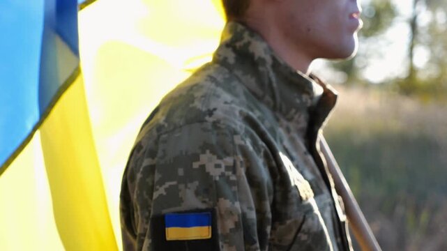 Ukrainian army man stands with national banner at countryside. Male soldier in military uniform with Ukraine flag as symbol of victory against russian aggression. Concept of invasion resistance