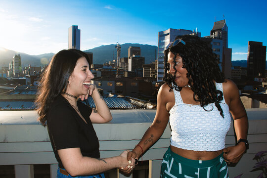 Two Women Shake Hands on a Rooftop With a City View in the Background